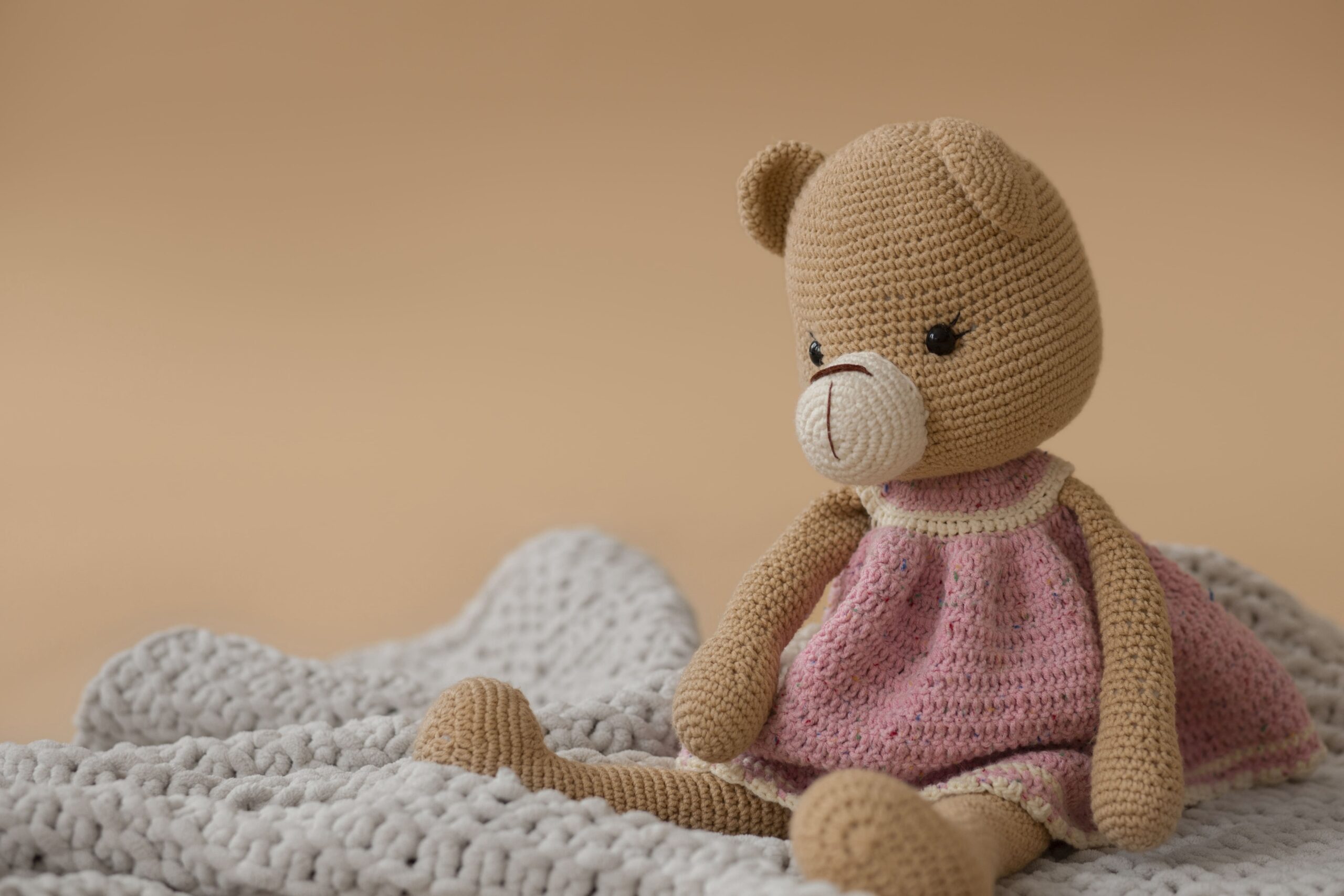 Unique BobblePoppz teddy bear in pink outfit sitting on a bed, representing cozy, one-of-a-kind custom toy design.
